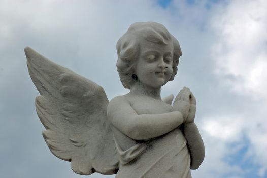 Stone carved statue of a cherub praying above a nineteenth century grave.