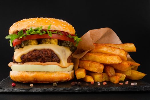 One big tall classic hamburger burger cheeseburger with french fries on black stone plate on black background with copy space for text