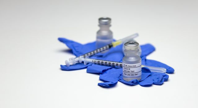 A pair of Covid-19 test vaccine vials on top of blue rubber medical gloves with syringes.