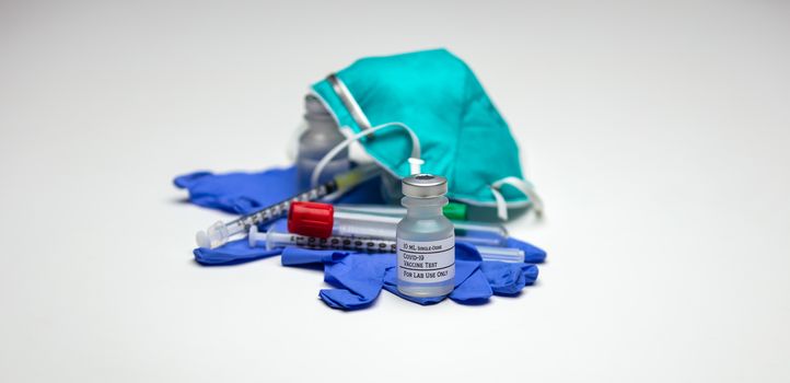 A vial of Covid-19 test vaccine on top of medical gloves, empty tube and N95 type respirator mask.