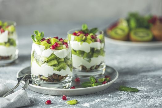 Two glasses healthy meal made of granola on gray plate, yogurt and kiwi fruits. Delicious food for breakfast. Traditional American snack.	