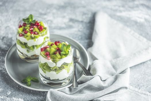 Two glasses healthy meal made of granola on gray plate, yogurt and kiwi fruits. Delicious food for breakfast. Traditional American snack.	