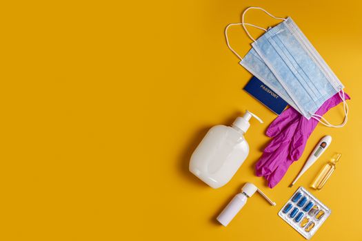 Coronavirus and travel concept. Passports, sanitizer, thermometer, medical gloves, surgical mask, sanitizer gel, blue capsules pill in blister and medical mask on yellow colored background, flat lay.