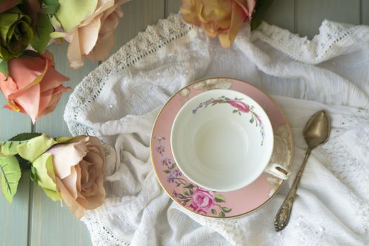 Vintage tea cup with gold rim. White linen tablecloth. Pastel roses, flat lay