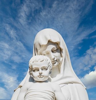 A white stone statue of the Madonna and Jesus under nice sky