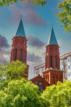 Steeple of an old red brick church with green metal roof under blue sky