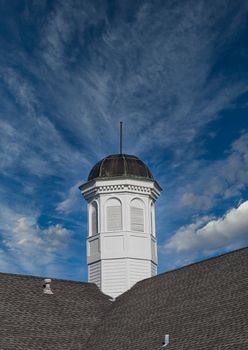 An old white wod cupola on a shingled roof under clear blue sky