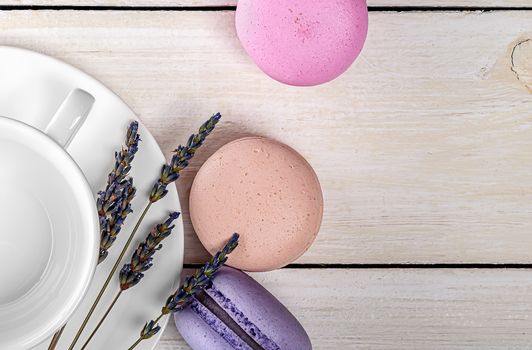 Multicolored macaroons near white coffee cup and lavender closeup top view on wooden table