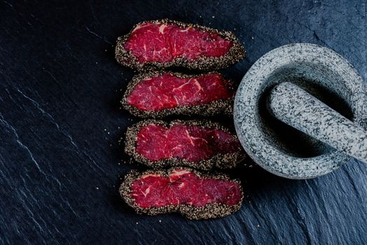 Pepper steaks on stone with mortar bowl and pestle above
