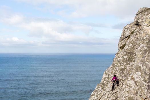 Woman climbing a cliff in the foreground with the sea in the background