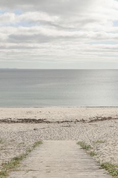 Board path to enter a beach without people and with a calm sea and cloudy sky