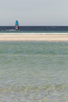 Windsurfer sailing near the sand of the beach with turquoise water in the foreground