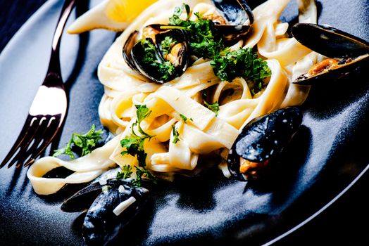 Blue mussels and pasta in black plate on stone surface close up