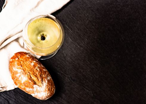 Glass with white vine and bread loaf on stone surface