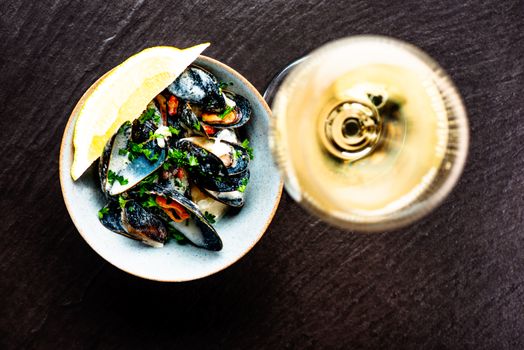 Cooked Blue mussels in clay dish next to white wine glass
