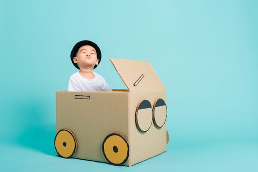 Happy Asian children boy smile in driving play car creative by a cardboard box imagination, summer holiday travel concept, studio shot on blue background with copy space for text