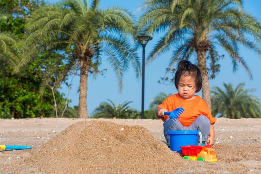 Asian Thai happy cute little cheerful Brother and sister two children funny digging play toy with sand at an outdoor tropical beach in summer day with copy space