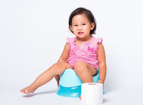 Asian little cute baby child girl education training to sitting on blue chamber pot or potty with toilet paper rolls, studio shot isolated on white background, wc toilet concept