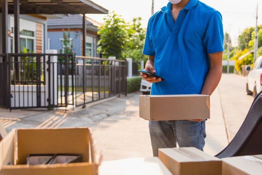 Asian delivery man courier moving deliveries out boxes in back car he protective face mask, service customer on front house under curfew quarantine pandemic coronavirus COVID-19, in car trunk view