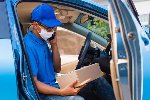 Asian delivery man courier online holding deliveries out boxes in car and using mobile phone contact the customer he protective face mask service under curfew quarantine pandemic coronavirus COVID-19