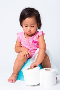 Asian little cute baby child girl education training to sitting on blue chamber pot or potty with toilet paper rolls, studio shot isolated on white background, wc toilet concept