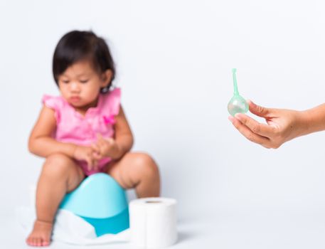 Asian little cute baby child girl training to sitting on blue chamber pot or potty her problem cannot shit and mother use Enema for help, studio shot isolated on white background, wc toilet concept