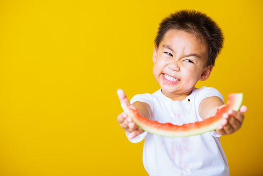 Happy portrait Asian child or kid cute little boy attractive laugh smile playing holds cut watermelon fresh for eating, studio shot isolated on yellow background, healthy food and summer concept