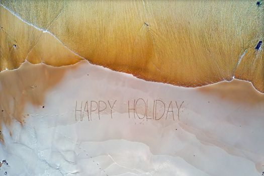 Aerial top shot from ocean waves and handwritten Happy holiday at the beach