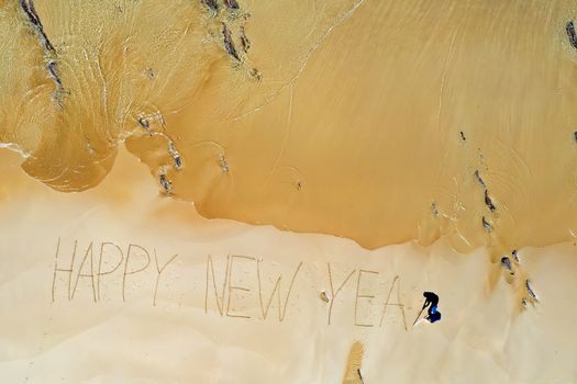 Aerial top shot from ocean waves and handwritten Happy New Year at the beach
