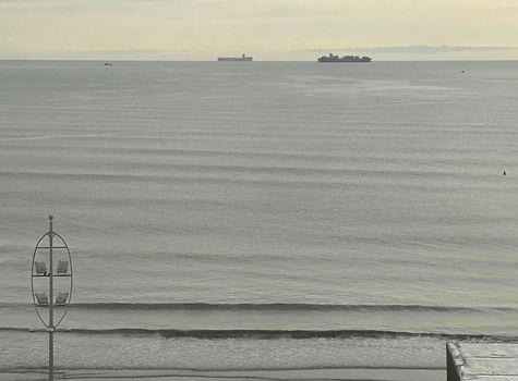 Beach coast with grayish sky, boats, calm sea, rainy sunrise