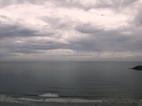 Beach coast with grayish sky, boats, calm sea, rainy sunrise