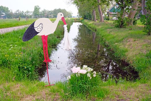 Design of a stork bringing a baby to a house in the countryside of the Netherlands