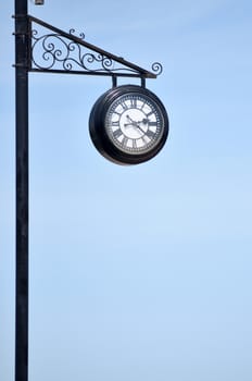 City clock on an iron pillar against a blue sky with Roman numerals.