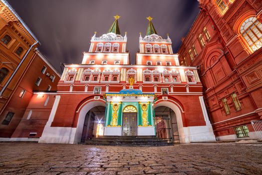 Evening photo of the Resurrection Gate in Moscow with illuminated buildings against moving clouds sky