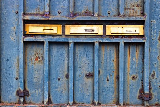 Rusty metallic door with three golden mail boxes 