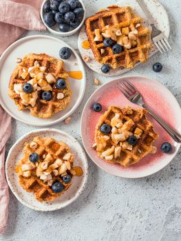 Easy healthy gluten free oat waffles with copy space. Plates with appetizing homemade waffles with oat flour decorated blueberries, bananas and honey on gray background. Vertical. Top view or flat lay