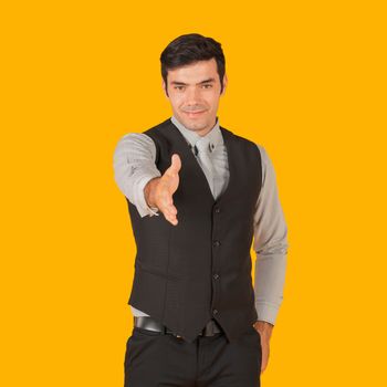 Young businessman in a gray shirt and black vest is ready to shake hands and start successful business project. Concept of business relationships. Portrait on yellow background with studio light.