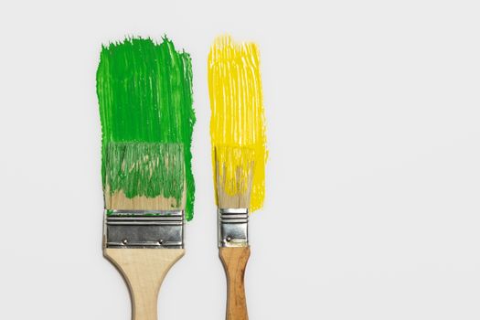 Paintbrushes and a trail of green and yellow paint in isolated background. Concept of painting, renovation, home and household chores