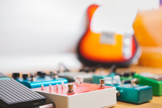 Guitar pedalboard on the floor of a recording studio, electric guitar in the background. Generic guitar effects on the wooden floor. Guitar recording, rock music creation concept