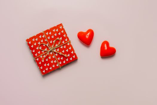 Gift wrapped in paper with a heart pattern and two hearts on a pink background, top view. Valentine's day concept, giving gifts and presents