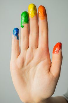 Close-up view of a hand with paint on the fingertips. Blue, green, yellow, orange and red paints on fingers, studio shot.