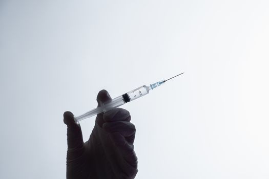 Injection ready for application, dark silhouette on white background. Hand in glove holding a syringe with intravenous injection, concept of vaccination or illegal medicine