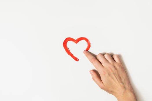 Finger draws a heart's shape with red paint on a white background. Charity, love or St. Valentines day concept.