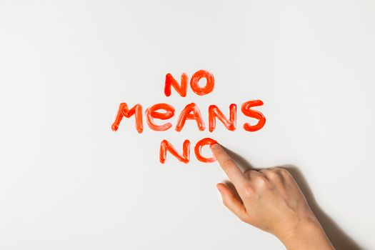 Women finger draws a phrase "No means no" with red paint on a white background. Sexual abuse, rape prevention and personal boundaries concepts.