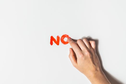 Woman finger draws a word "No" with red paint on a white background. Sexual abuse, rape prevention and personal boundaries concepts.