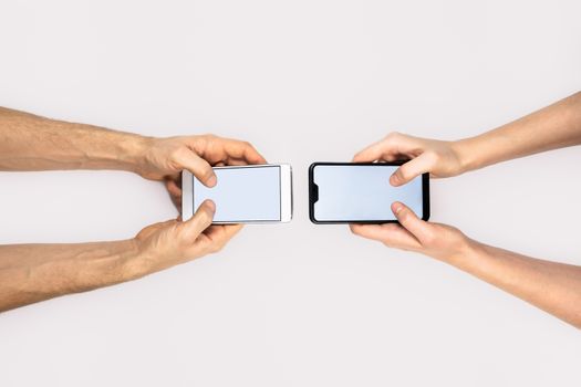 Female and male hands hold smartphones on white background with copy space. Messaging, texting, communication concept