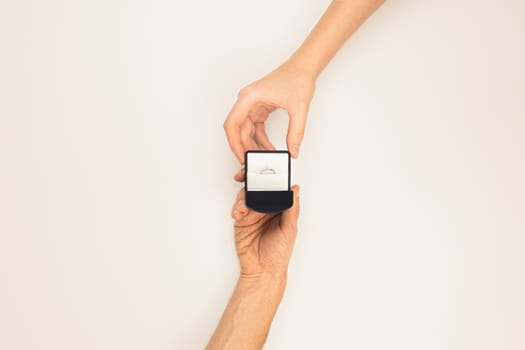 Hand giving a box with a wedding ring to the other hand on white background, top view. 
Marriage proposal concept