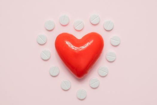 Heart and pills in the shape of a heart on pink background, top view. Cardiology, heart disease concept.