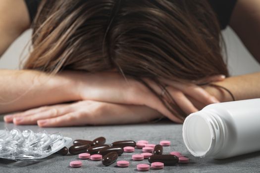 Concept of drugs abuse. Female with her head on the table in front of pills and prescription substances, concept of depression or suicide attmept