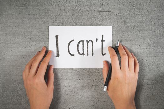 Hands with a pen and sign "i can't" on the paper. Motivational concept, writing a note, disbelief in yourself or lack of self confidence concept.